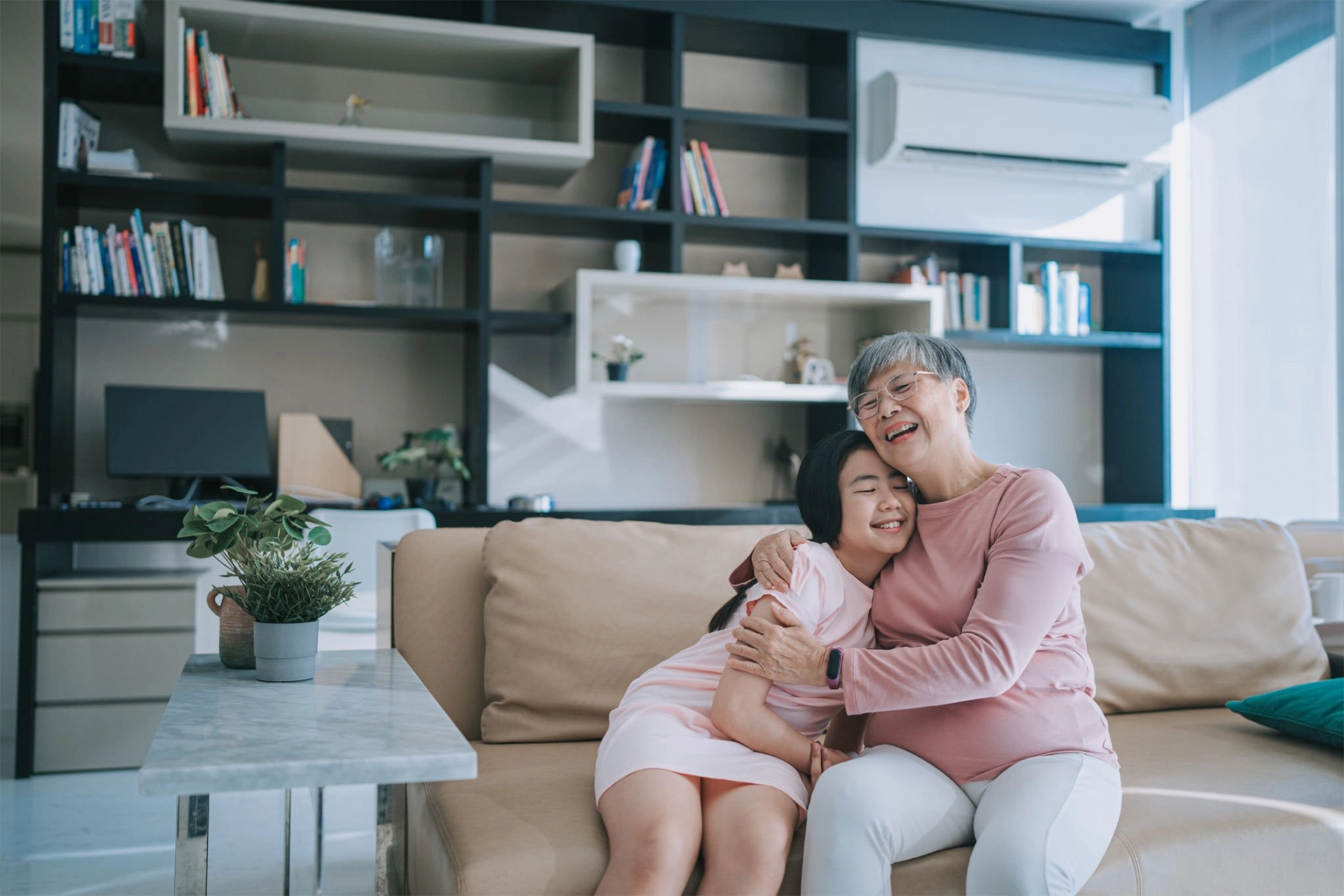 Happy chinese grandmother hugging her granddaughter in living room