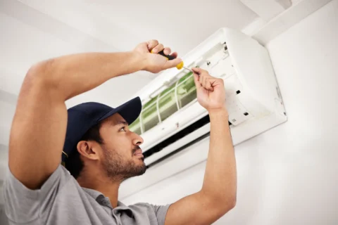 Man in gray shirt unscrewing air conditioner filter